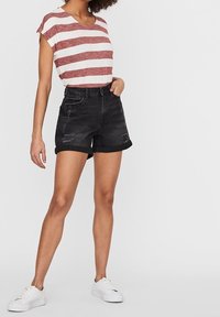 Červeno-bíle pruhované tričko s krátkým rukávem, spárované s černými džínovými šortkami s prošlapanými detaily, nošeno s bílými teniskami.