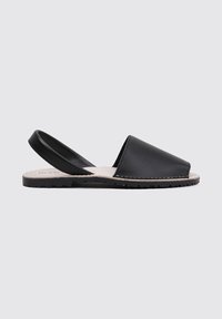 Sandalia negra de piel, tipo slingback, con puntera cerrada, suela plana de goma y detalles cosidos a lo largo del borde. Textura suave, diseño sencillo.