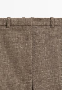 Ceinture en tissu marron texturé avec passants de ceinture et une couture centrale d'un pantalon.