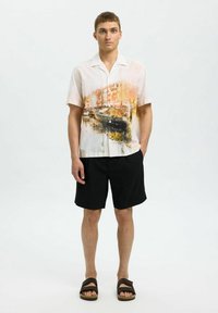 Krátký rukáv košile na knoflíky z lehké látky s abstraktním oranžovo-černým potiskem. Kombinováno s černými šortkami a hnědými sandály.