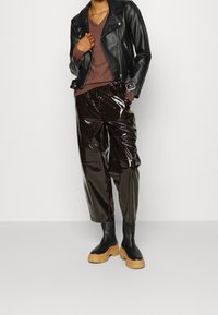 Svart läderbikerjacka, brun v-ringad tröja, blanka svarta kapade byxor och kraftiga svarta stövlar med träplattformsåhlar.