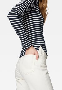 Námořnický modrý a bílý pruhovaný top s dlouhým rukávem a přiléhavým střihem, bočními rozparky, kombinovaný s bílými džínami s vysokým pasem a zadními kapsami.