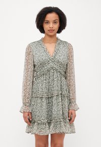 Green floral dress with sheer long sleeves, ruffled details, and layered tiers. Features a v-neckline and a pattern of white leaves.