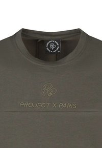 Camiseta verde oliva hecha de una tela suave con cuello redondo; presenta el texto bordado "PROJECT X PARIS" en un color a juego. Etiqueta visible.