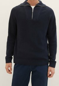 Pullover in maglia colore navy con collo a zip parziale, dettagli testurizzati sulle spalle, polsini e orlo a costine. Tessuto morbido di peso medio.