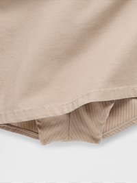 Beige bomullsstoff med en subtil diagonalt tekstur, med en kant som har en rett kant og minimal sømdekorasjon.