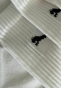 Weißer, gerippter Stoff mit kleinen schwarzen Gitarrenmotiven, die in das Material eingewebt sind, in einer Nahaufnahme gezeigt.