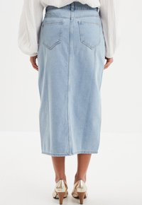 Falda midi de mezclilla azul claro con corte recto, bolsillos traseros y una costura en el centro. Combinada con zapatos de tacón dorados brillantes.