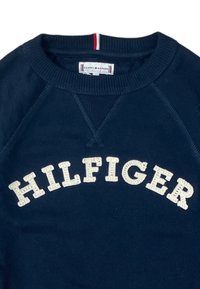 Felpa blu navy con collo a costine, con testo ricamato "HILFIGER" in crema. Include un accento rosso, bianco e blu sul colletto.