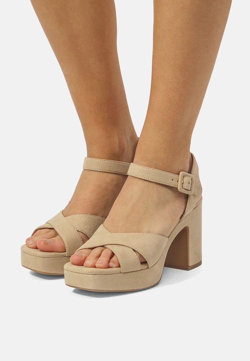Sandalias de plataforma beige con tacón cuadrado, que presentan correas cruzadas y una correa ajustable en el tobillo de textura suave de ante.