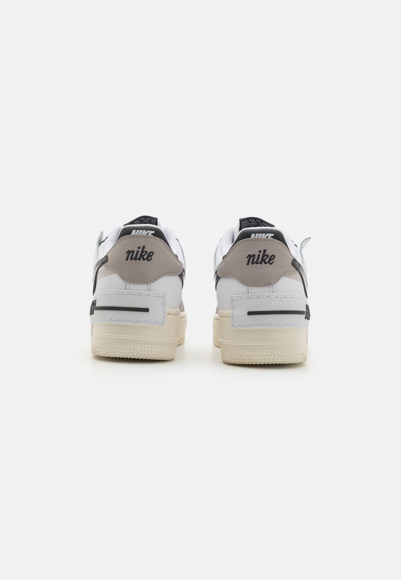 Zapatillas Nike con un upper de cuero blanco, acentos en gris y una suela gruesa de color crema; marca negra en el talón y la lengüeta.