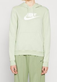 Person som bär en ljusgrön Nike-hoodie med vit logga och matchande ljusgröna byxor med liten svart Nike-swoosh.
