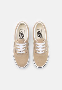 Béžové plátěné tenisky s bílými tkaničkami, gumovou podrážkou a černým kontrastním prošitím. Klasický design, který nabízí jednoduchý a univerzální vzhled.