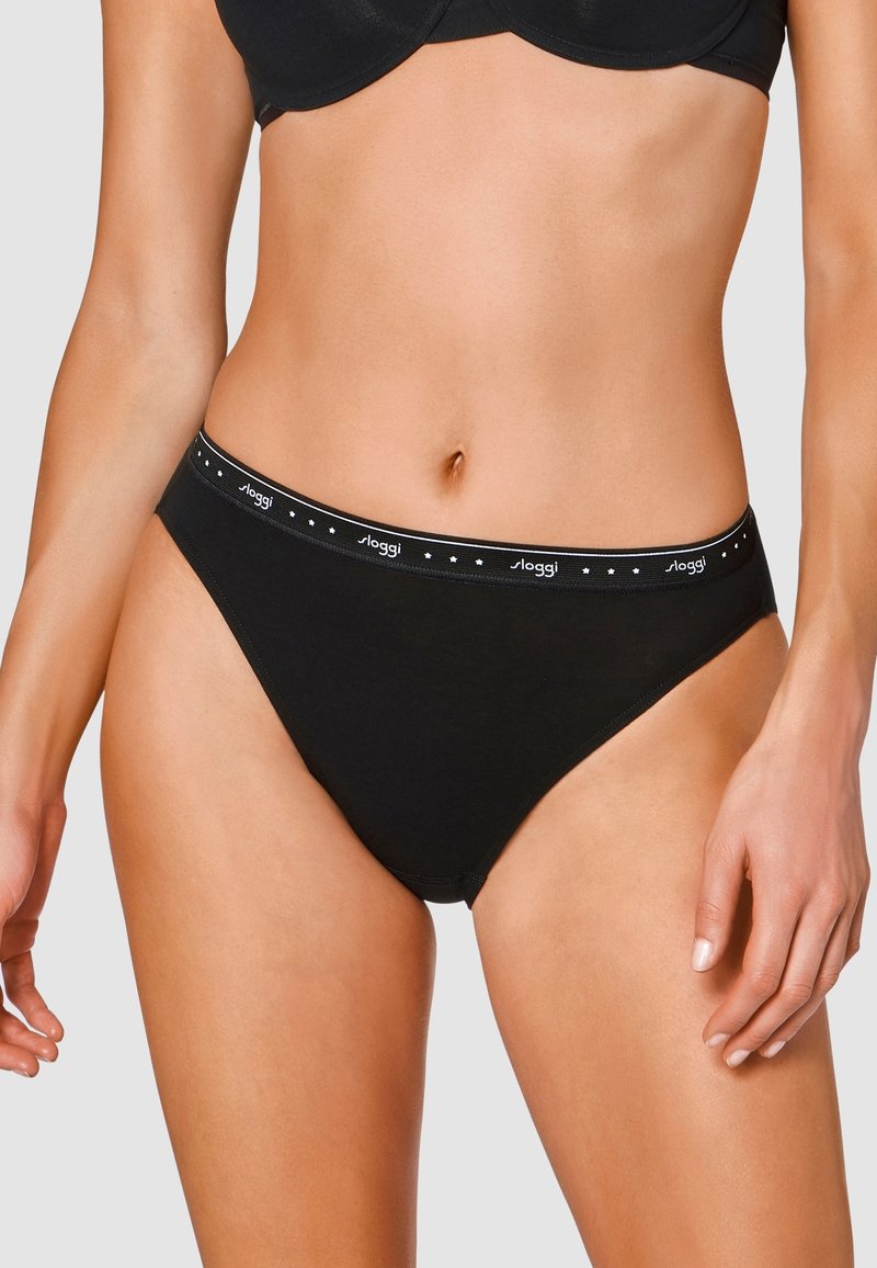 Slip in cotone nero con una larga cintura elastica caratterizzata da piccoli pois bianchi. Il design presenta un taglio classico e una texture liscia.