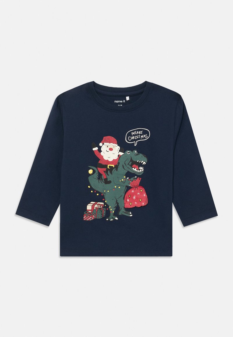 Tengerészeti hosszú ujjú póló, amelyen egy dinoszauruszon ülő Mikulás grafikája látható, karácsonyi ajándékokkal és fényekkel körülvéve. Puha pamut anyag.