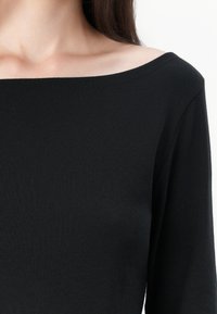Top nero senza spalle realizzato in tessuto a coste, con maniche lunghe e scollatura ampia, che mette in mostra una texture liscia e un design aderente.
