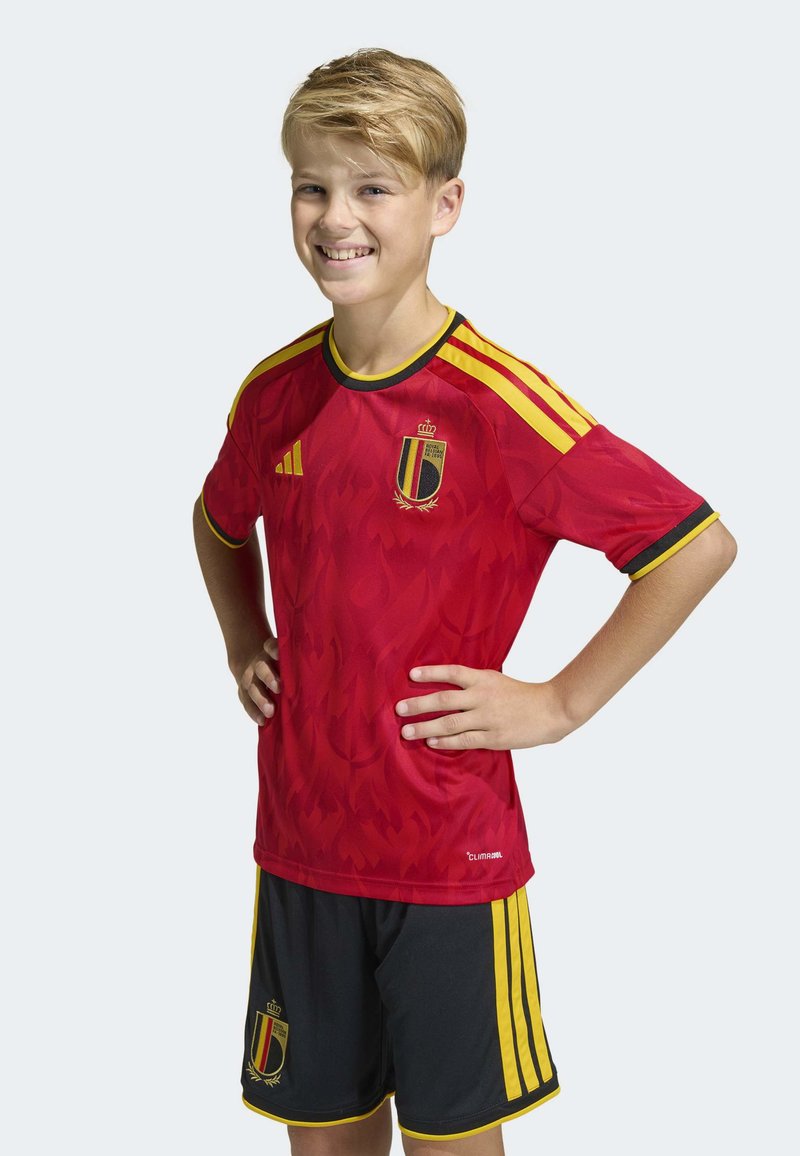 Röd fotbollströja med gula detaljer och svart kant, med ett subtilt flammande mönster och Belgiens emblem. Svarta shorts med gula ränder.