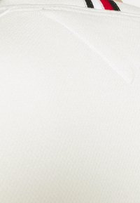 Weißer strukturierter Stoff mit einem diagonalen Muster und schwarzen, roten und weißen Streifen entlang des oberen Randes.