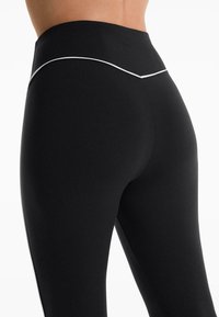 Black high-waisted leggings made from stretchy material. Features a contrasting white accent line along the waistband. Seamless design.