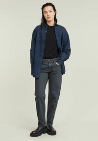 Camicia in denim blu scuro, t-shirt nera, pantaloni grigi e stivaletti neri chunky. Presenta chiusura con bottoni, maniche lunghe e vestibilità rilassata.