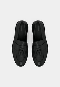 Svarta läderloafers med en jämn textur, utrustade med ett främre band och dekorativa tofsar. Minimalistisk design med en låg profil.