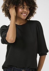 Svart kortärmad topp i mjukt tyg med volangärmar och rundad halsringning. Slät textur med en avslappnad passform.