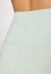 Világos zöld, magas derekú leggings, sima textúrával, minimális varrással és egy kis, dombornyomott logóval a derékpánt közelében.