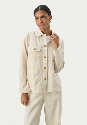 Veste en lin beige clair avec col, ornée de boutons en bois et de deux poches avant. Le tissu a une finition texturée.