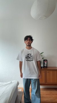 Bílý tričko s černým grafickým potiskem obsahujícím text a hvězdy. Spárováno s volnými světle modrými džíny. Jednoduchý, ležérní design.