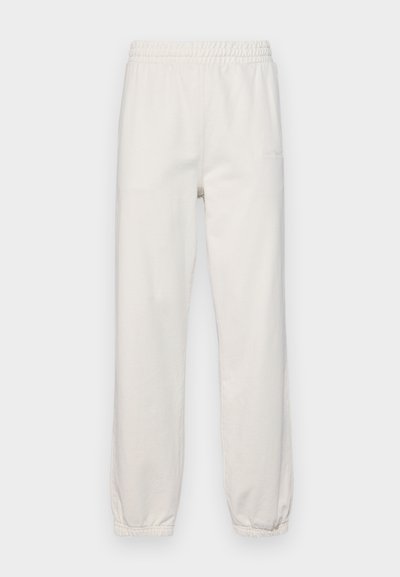 Light beige sweatpants with an elastic waistband, tapered legs, and a brushed cotton texture. Features a logo on the front.
