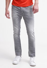 Šedé džíny z denimu s mírně vybledlým povrchem, slim fit, pět kapsový design a červené švy, nošené s bílými teniskami.
