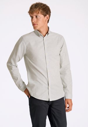 Camisa de botones a rayas en verde claro y blanco, hecha de una tela de textura suave. Presenta un cuello y mangas largas, combinada con pantalones negros.