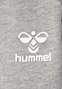 Grå sweatshirt med en vit gummiprintlogotyp med symmetrisk design och ordet "hummel" tryckt nedanför. Mjuk, strukturerad och texturerad tyg.