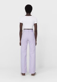 Jean de pierna ancha de color púrpura claro, confeccionado en denim, con una cintura alta y dos bolsillos traseros. Combinado con una camiseta corta blanca.