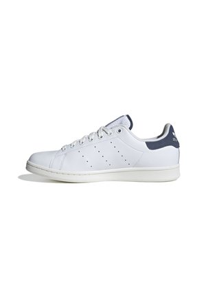 Baskets basses blanches avec des lacets blancs, un motif latéral perforé, et un onglet talon bleu foncé avec logo sur fond blanc.