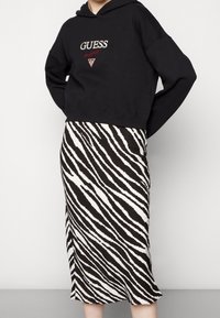 Svart croppad hoodie med "GUESS"-logotyp; ihop med en knälång zebra-mönstrad kjol i svart och vitt. Släta texturer, avslappnad design.