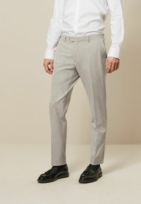 Pantalons tailleur gris clair avec une texture lisse, coupe ajustée, passants de ceinture et fermeture à bouton unique. Associés à des mocassins noirs.
