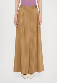 Wide-leg, high-waisted trousers in a mustard fabric with thin vertical stripes. Features pleats and a smooth texture. Paired with cream-colored shoes.