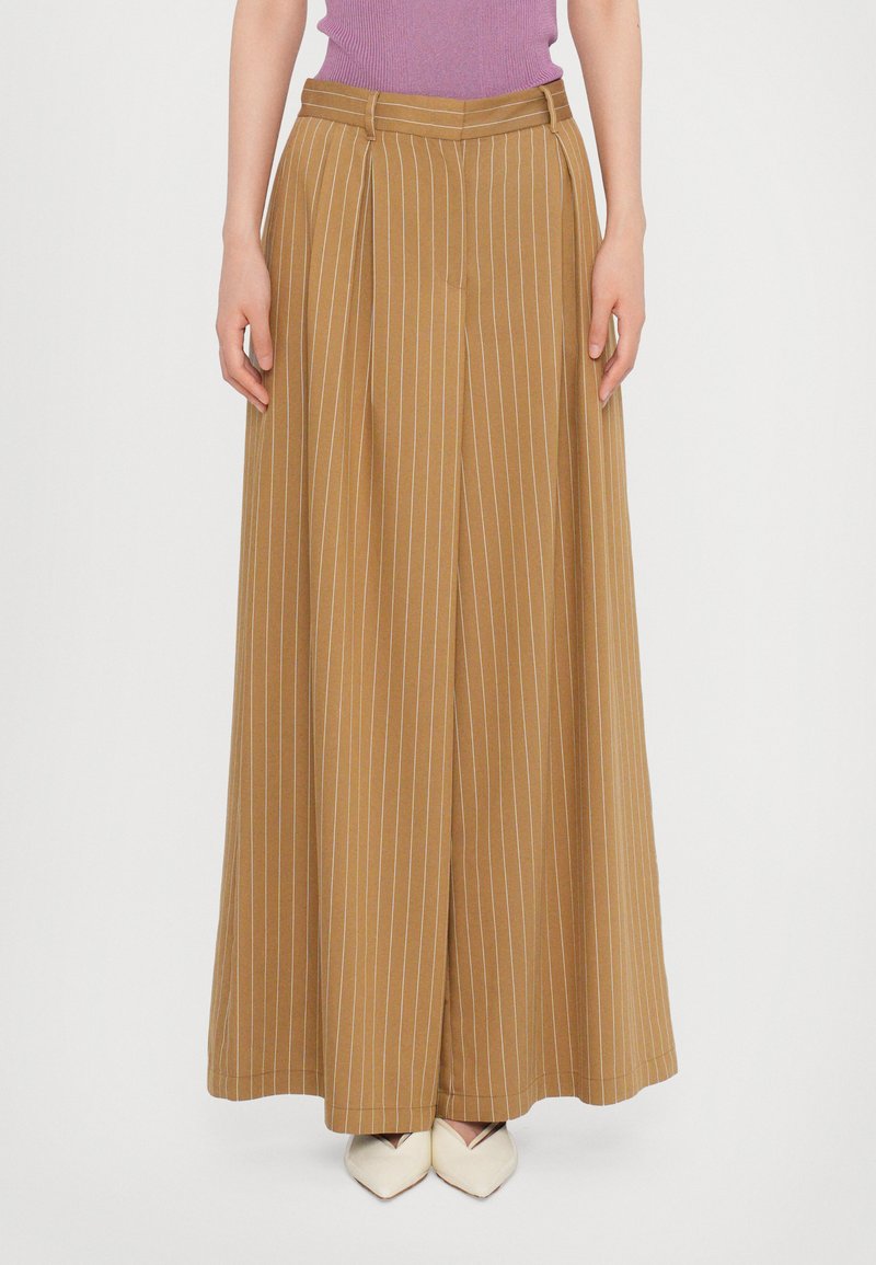 Wide-leg, high-waisted trousers in a mustard fabric with thin vertical stripes. Features pleats and a smooth texture. Paired with cream-colored shoes.