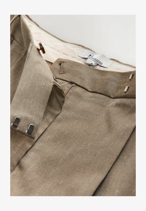 Braune Stoffhosen mit vertikalen Nadelstreifen, ausgestattet mit einem Reißverschluss, Knopfverschluss und Metallbeschlägen. Innenlabels sichtbar.