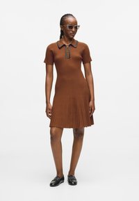 Pruunist ribikleidist, millel on lühikesed varrukad, krae ja kolm nuppu. Kleidil on volditud seelik ning see on kombineeritud mustade loafer'itega ja päikeseprillidega.