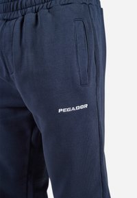 Navy blue sweatpants made of cotton blend, featuring an elastic waistband and side pockets. "PEGADOR" is embroidered in white on the thigh.