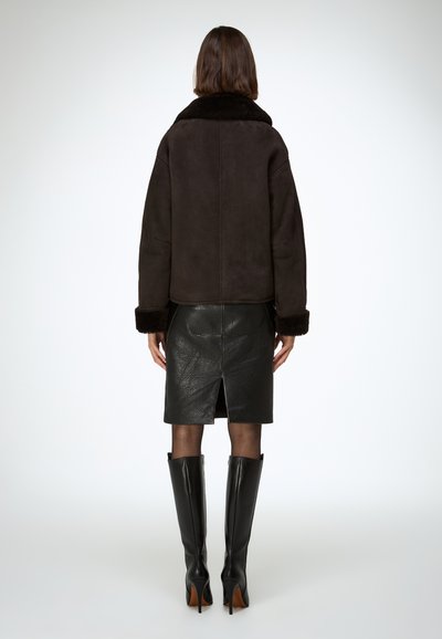 Ciemnobrązowa zamszowa kurtka z futrzanym kołnierzem, zestawiona z czarną skórzaną ołówkową spódnicą z rozcięciem z tyłu. Czarne kozaki na obcasie sięgające do kolan.