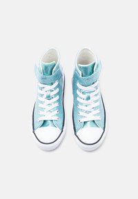 Paari läikivaid türkiissiniseid kõrgete säärega tossusid valgete paelte ja kummist tallaga, vaadatuna ülevalt helel taustal.