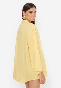 Κίτρινο, ελαφρύ, φαρδύ πουκάμισο με μακριά μανίκια, άνετη εφαρμογή και λεία υφή, σχεδιασμένο με πλαϊνές σχισμές.