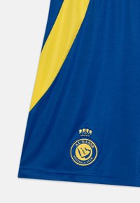 Zila futbola krekls ar dzelteniem akcentiem, ar izšūtu apļa kluba logo apakšā, izgatavots no elpojoša materiāla.