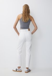White jeans with a high waist, straight leg, and two back pockets. Paired with a gray sleeveless top and white sneakers with black accents.