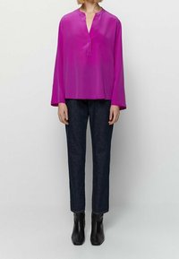 Blouse à manches longues en popeline de couleur rose vif, associée à un pantalon en denim foncé. Des bottines noires à la cheville complètent la tenue. Texture lisse et coupe décontractée.