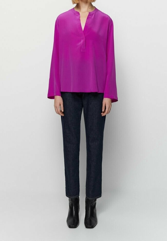 Blouse à manches longues en popeline de couleur rose vif, associée à un pantalon en denim foncé. Des bottines noires à la cheville complètent la tenue. Texture lisse et coupe décontractée.