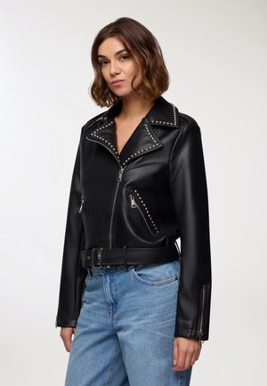 Giacca in ecopelle nera con rever affilati, dettagli borchiati lungo il collo e tasche con zip. Presenta una vita cintata e un design aderente.